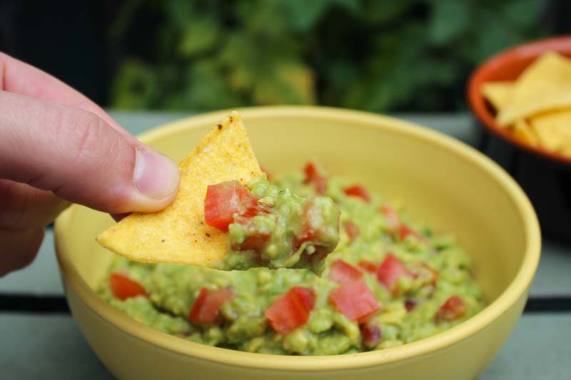 Dipping Tortilla Chip into Guacamole with Tomatoes